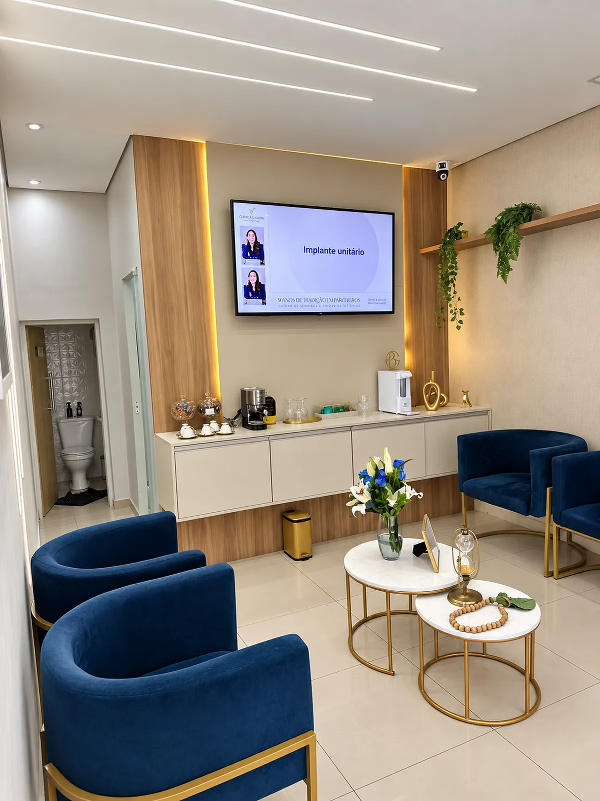 Sala de espera com poltronas azuis, mesa de centro com flores e bancada de exposição